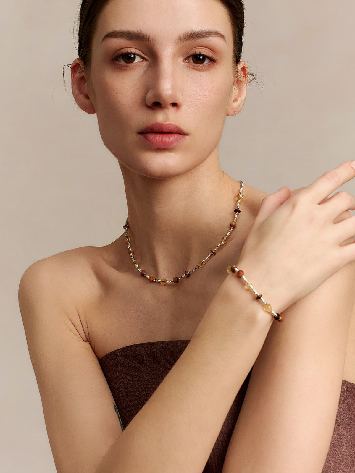 Model facing the camera, wearing the Fairyokai Soft Pure Light tay wood crystal braided necklace and a matching bracelet, with her right hand resting on her left shoulder, on neutral background.