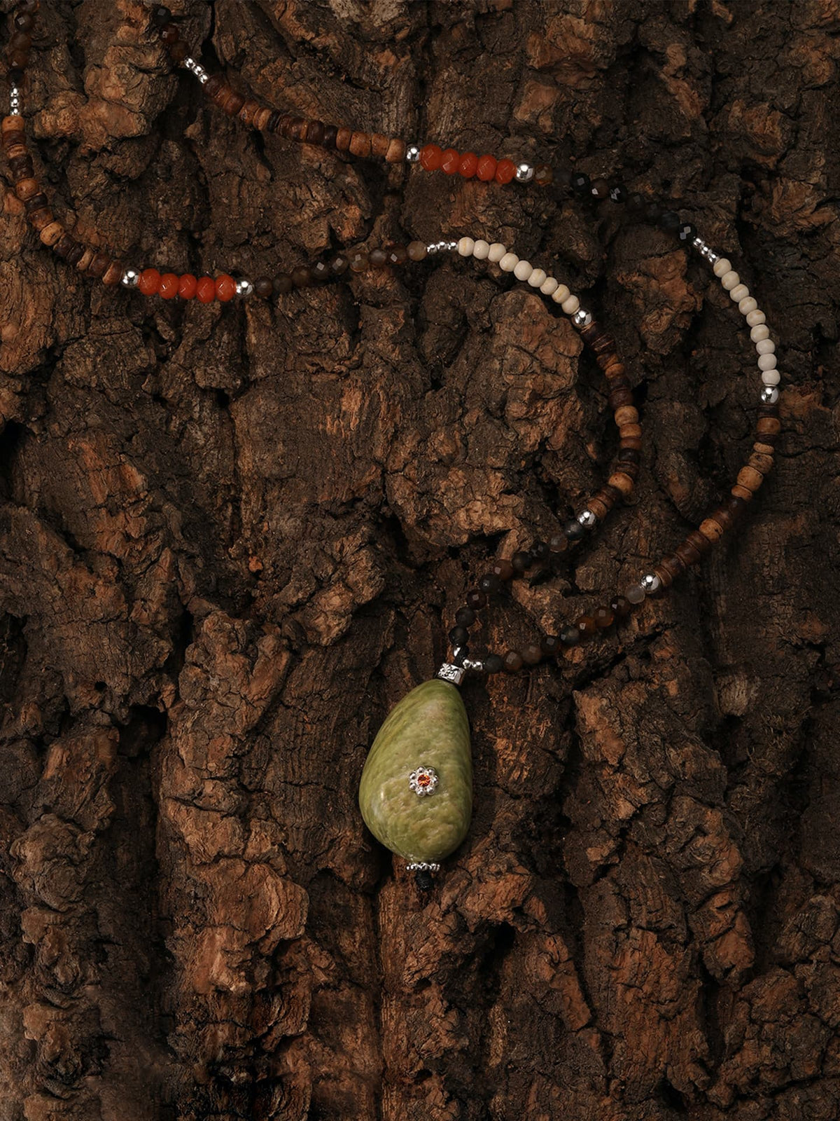 Fairyokai Spring Sequence multicolor avocado necklace with a green pendant, on a textured brown surface