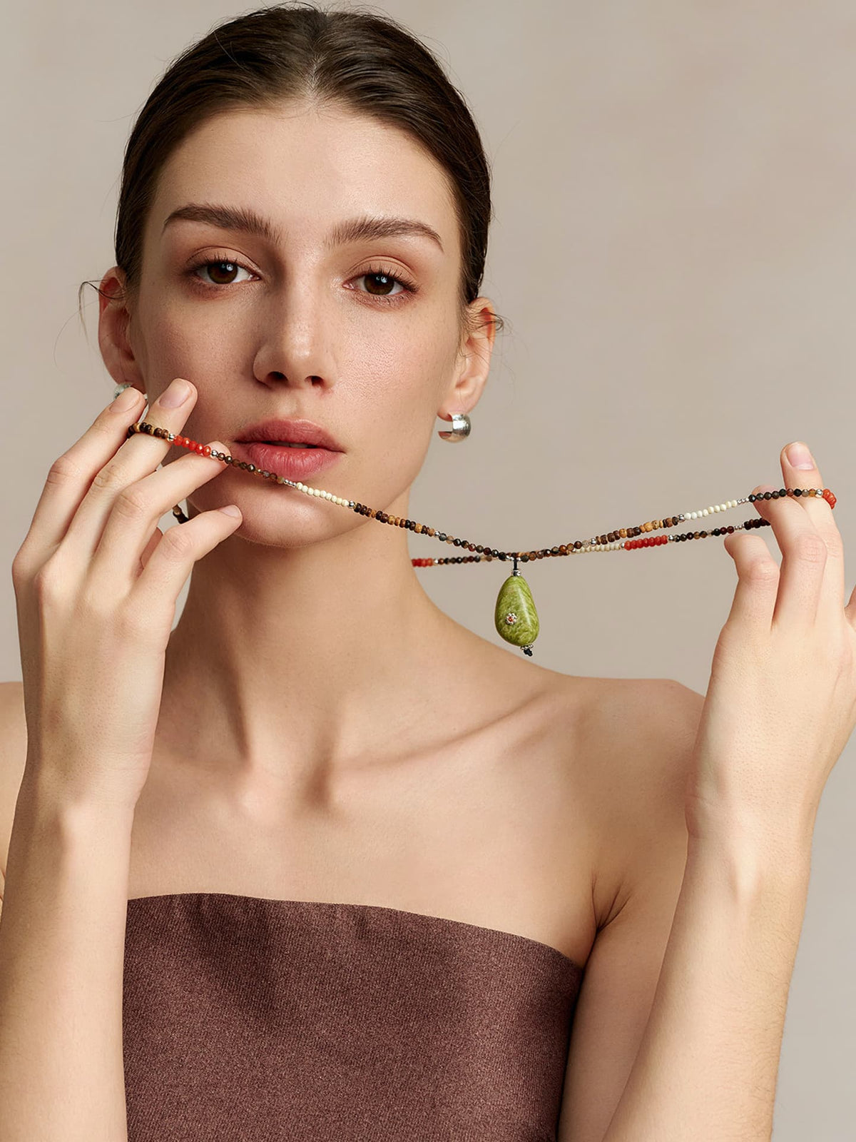 Model in a strapless top holding the Fairyokai Spring Sequence multicolor avocado necklace with both hands, facing the camera, on neutral background.