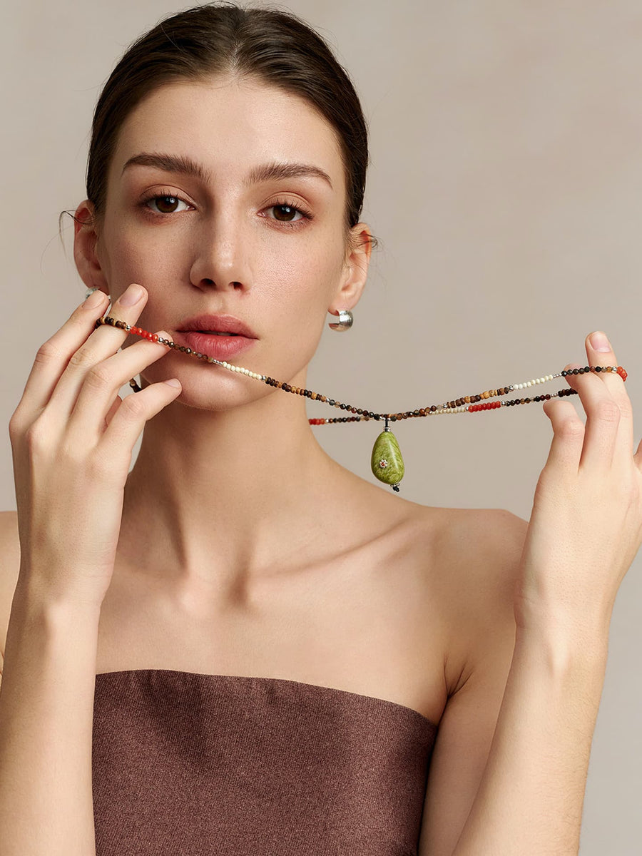 Model in a strapless top holding the Fairyokai Spring Sequence multicolor avocado necklace with both hands, facing the camera, on neutral background.