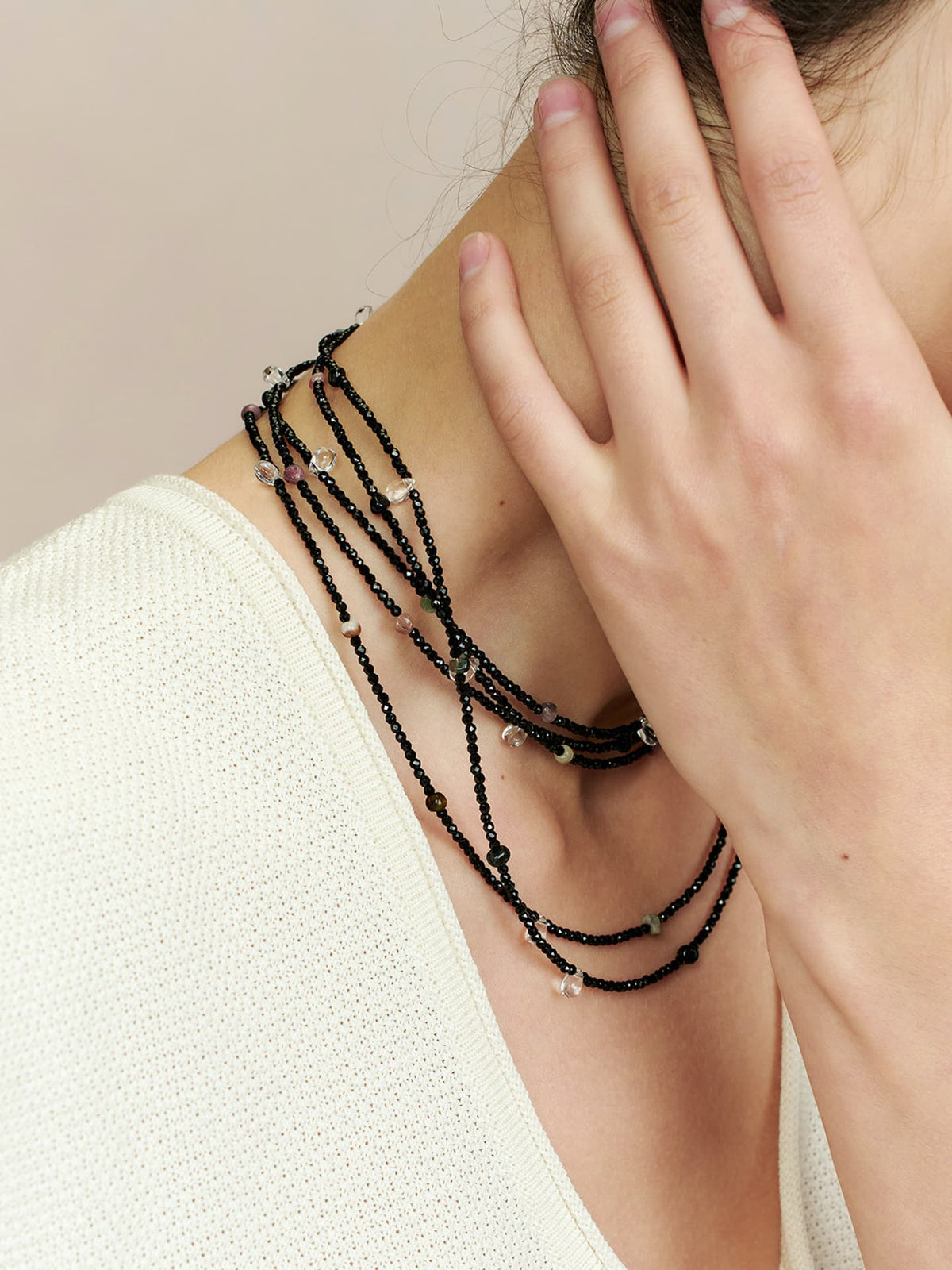 Close-up of a model in a white top wearing Fairyokai Starlight Chain multi-layer necklace wrapped around her neck, with her hand touching the necklace.
