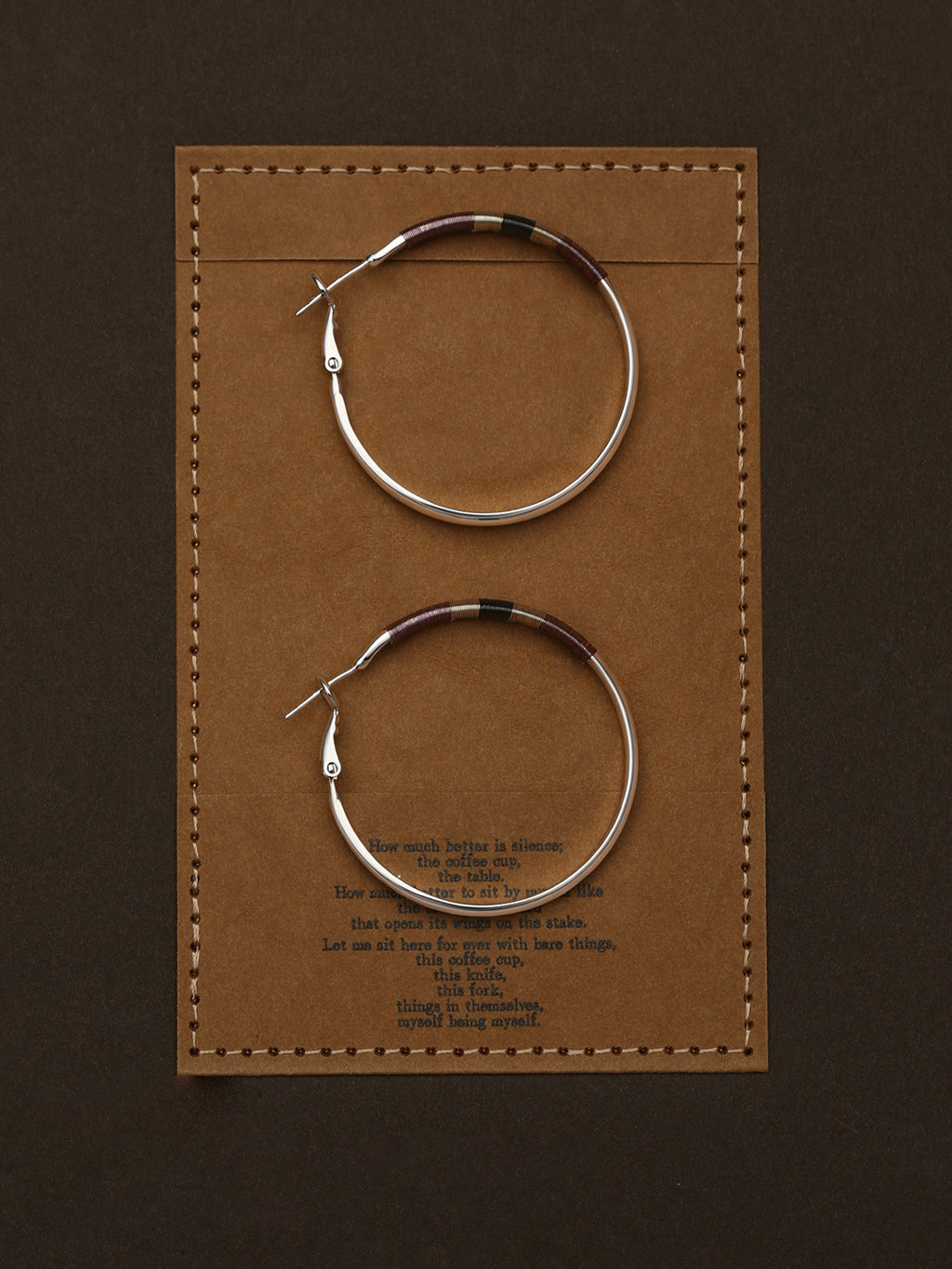 Pair of Fairyokai Three Color Thread Hoop Earrings — flatlay showing tricolor thread detail on hoop earrings, on a brown leather card with text.
