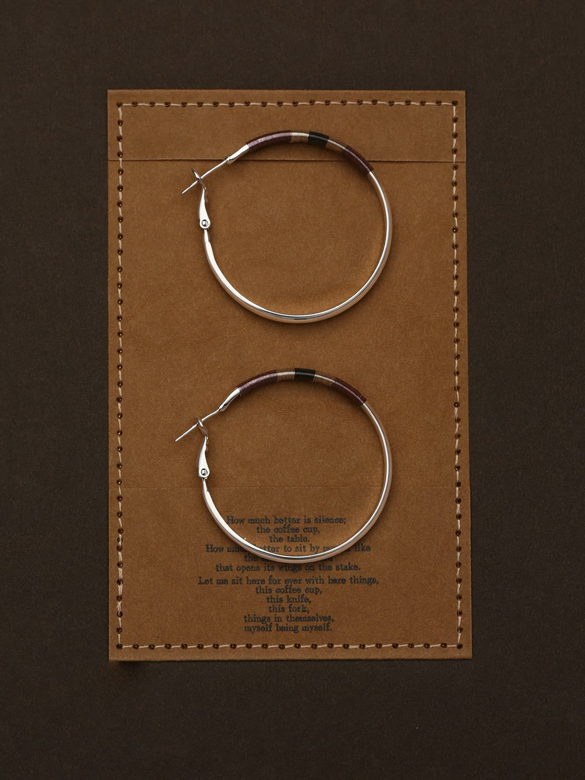 Pair of Fairyokai Three Color Thread Hoop Earrings — flatlay showing tricolor thread detail on hoop earrings, on a brown leather card with text.