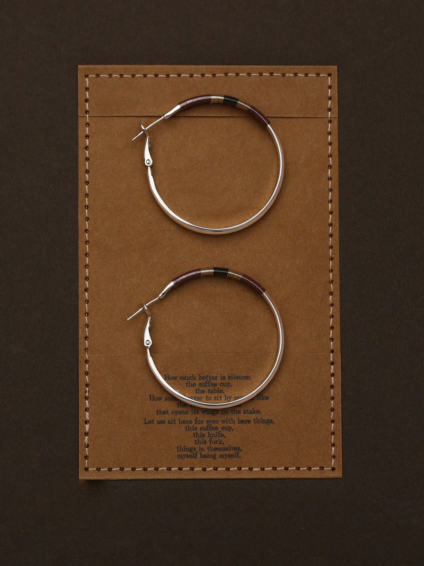 Pair of Fairyokai Three Color Thread Hoop Earrings — flatlay showing tricolor thread detail on hoop earrings, on a brown leather card with text.