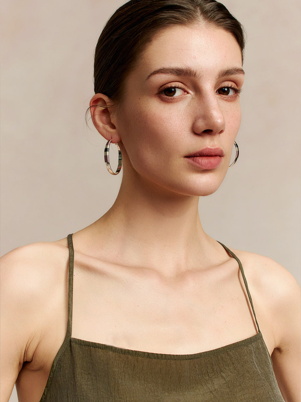 Model in a deep green thin-strap dress wearing Fairyokai Three-Color Thread hoop earrings, face slightly turned to the left while looking at the camera, against a beige background