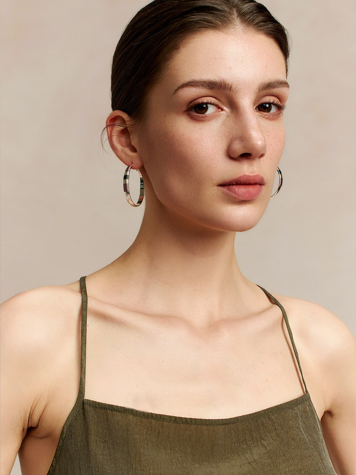 Model in a deep green thin-strap dress wearing Fairyokai Three-Color Thread hoop earrings, face slightly turned to the left while looking at the camera, against a beige background