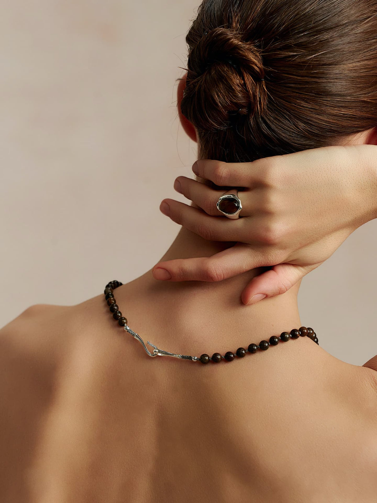 Close-up of a model wearing Fairyokai Tiger Eye and Silver Heart necklace from behind, with her hand touching the back of her neck, highlighting the necklace and her hand.