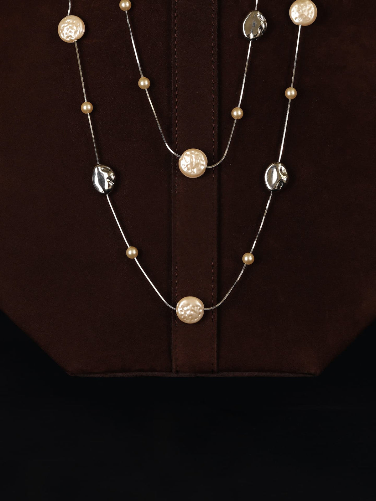 Fairyokai Tracing Light irregular faux pearl lobster clasp necklace draped over a dark brown bag against a black background.