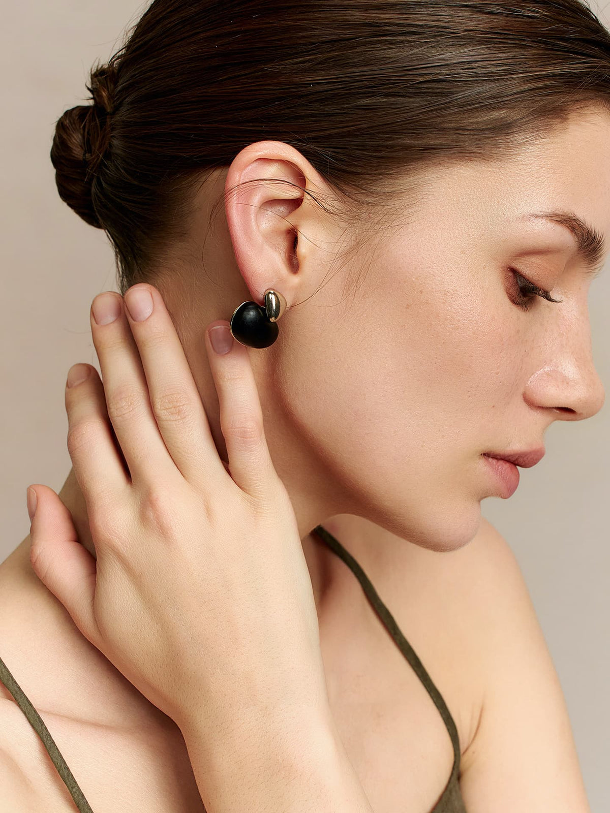 Close-up of a model in a deep green thin-strap dress, right hand touching her neck and the Fairyokai Quiet Leaf silver disc and ebony leaf earring, focusing on her right profile, side view on a neutral background