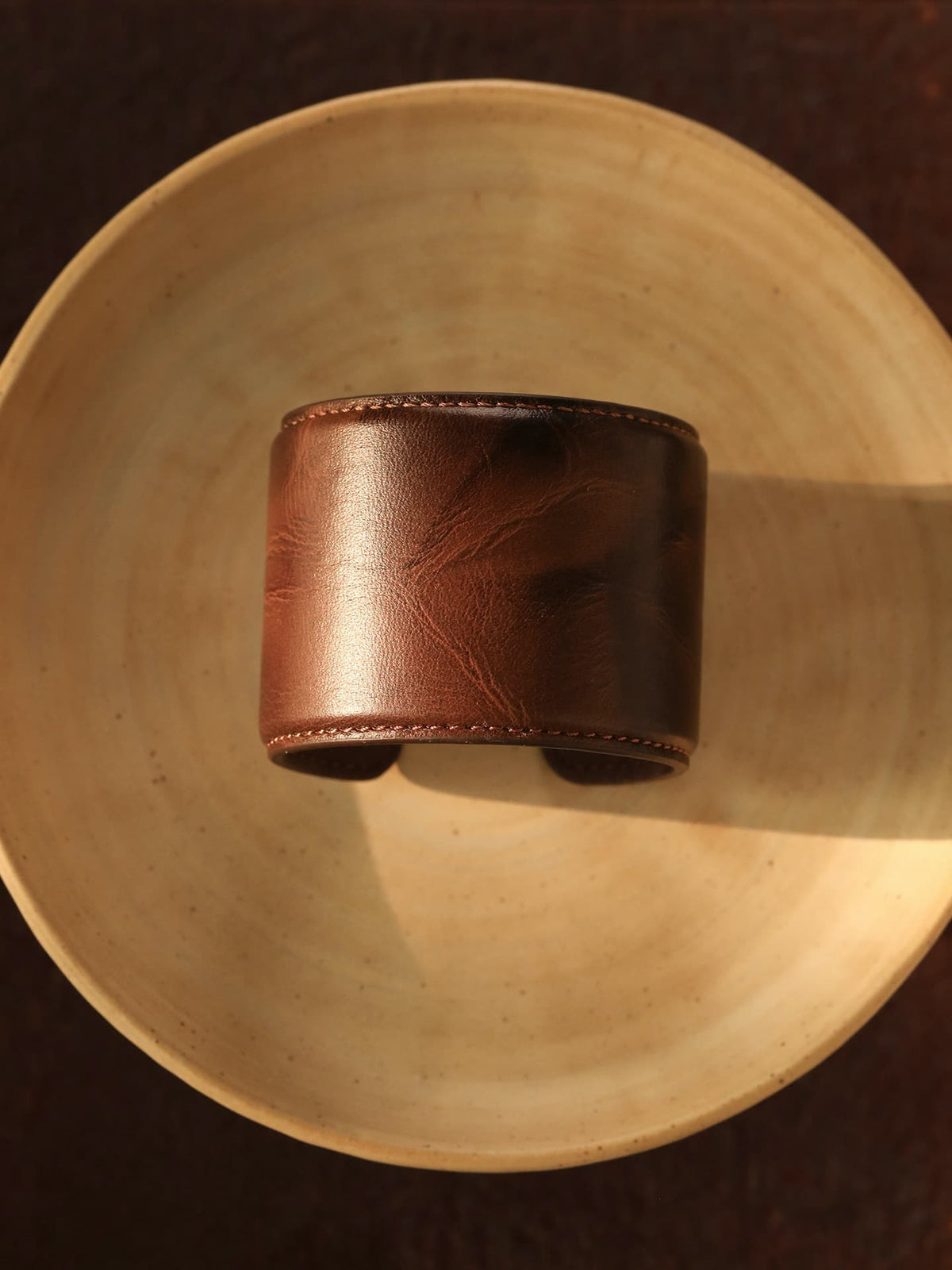 Fairyokai Vein Cuff PU leather bracelet set flat-laid on a wooden plate, showing the warm brown leather texture and wide cuff shape.