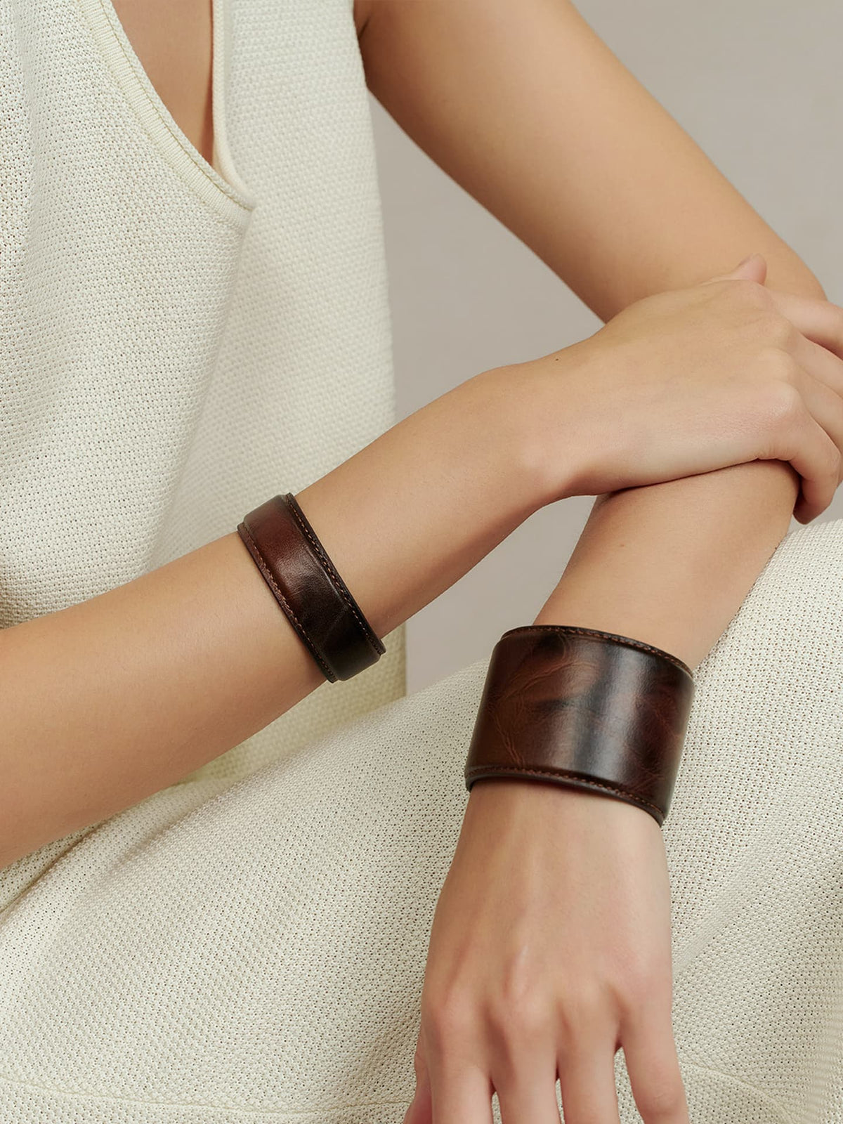 Close-up of a model wearing the Fairyokai Vein Cuff PU leather bracelet set, with two dark brown cuffs on crossed wrists.