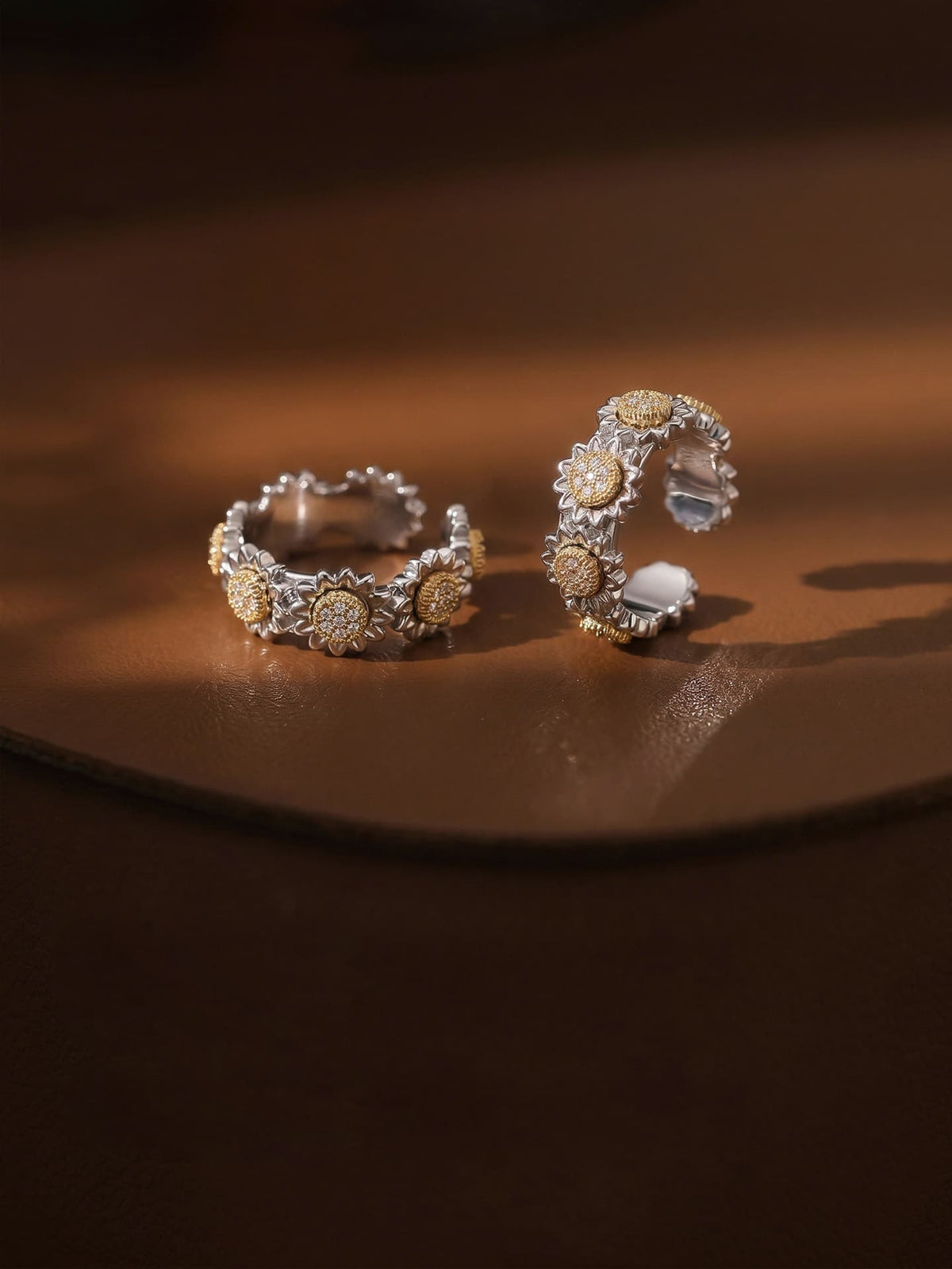 Fairyokai Wild Daisy gold textured zircon rings arranged on a warm brown surface, with soft light highlighting the floral texture.