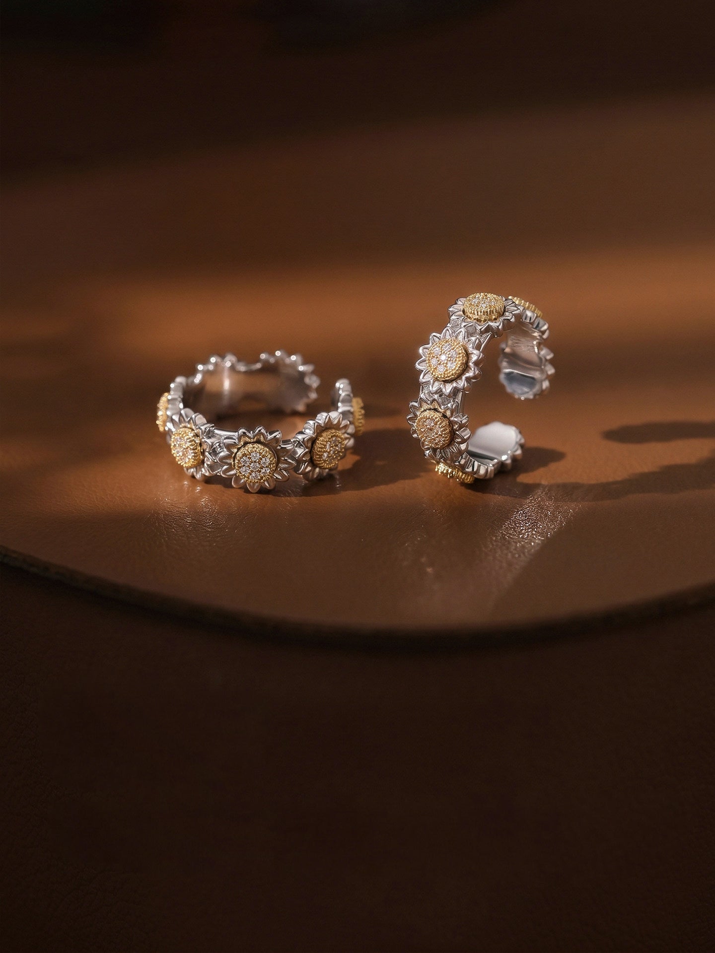 Fairyokai Wild Daisy gold textured zircon rings arranged on a warm brown surface, with soft light highlighting the floral texture.
