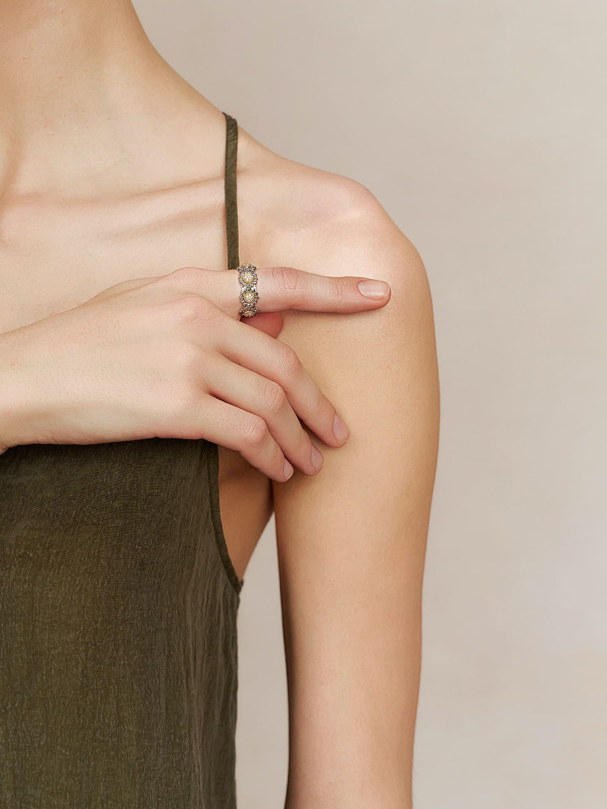 Model wearing the Fairyokai Wild Daisy gold textured zircon ring on a hand resting near the shoulder strap of an olive dress.