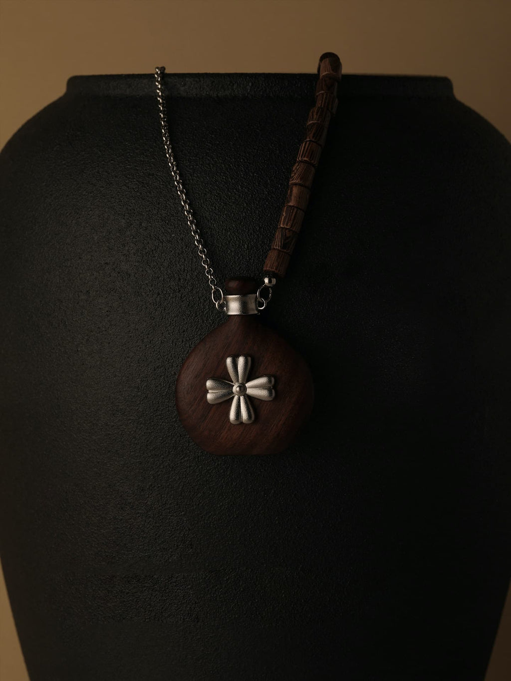 Fairyokai Wooden Serenity wenge wood vase necklace hanging on a black display stand, close-up detail.