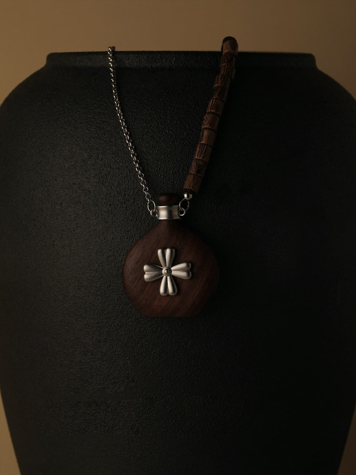 Fairyokai Wooden Serenity wenge wood vase necklace hanging on a black display stand, close-up detail.