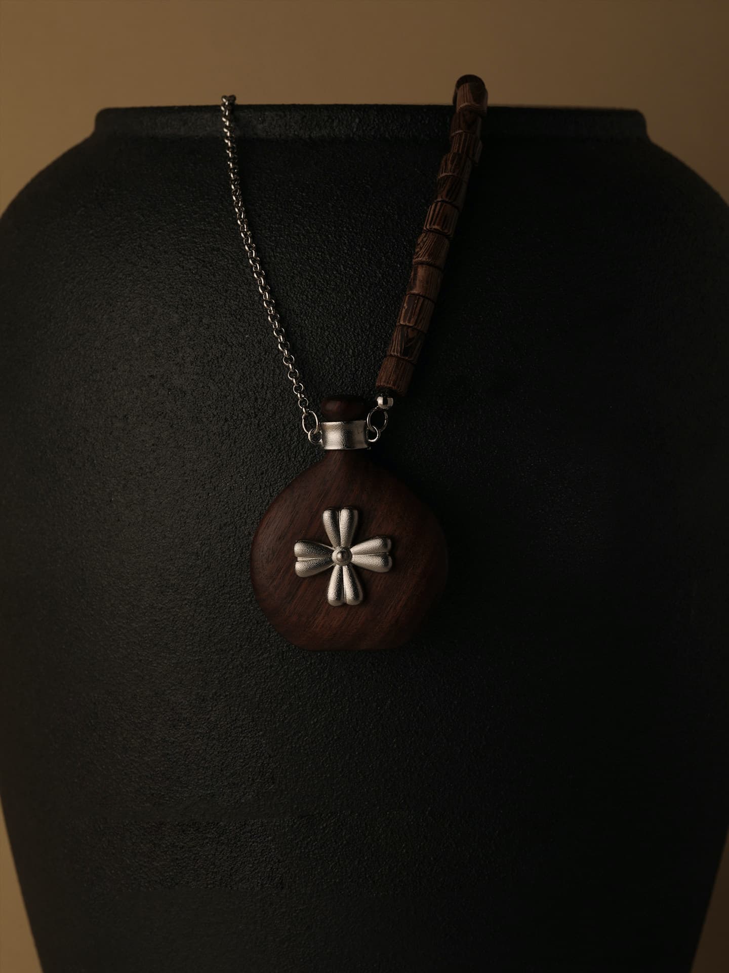Fairyokai Wooden Serenity wenge wood vase necklace hanging on a black display stand, close-up detail.